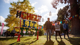 Four people walk past a #CheltLitFest sign, smiling. Four people walk past a #CheltLitFest sign, smiling.